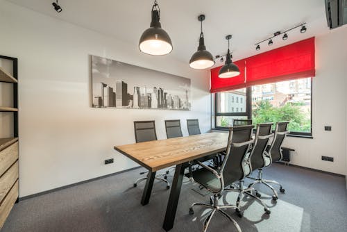 Wooden table with comfortable chairs in modern spacious conference hall with creative lamps and jalousie on windows