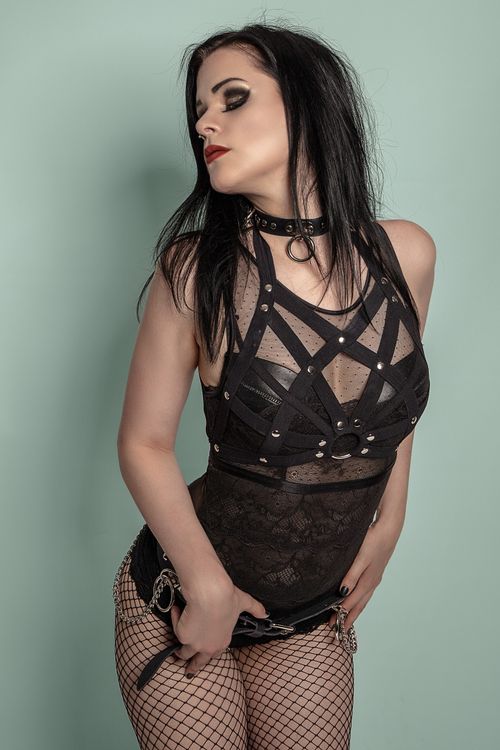 Free A gothic fashion model poses in fishnet tights and a choker, embodying edgy elegance in a studio setting. Stock Photo