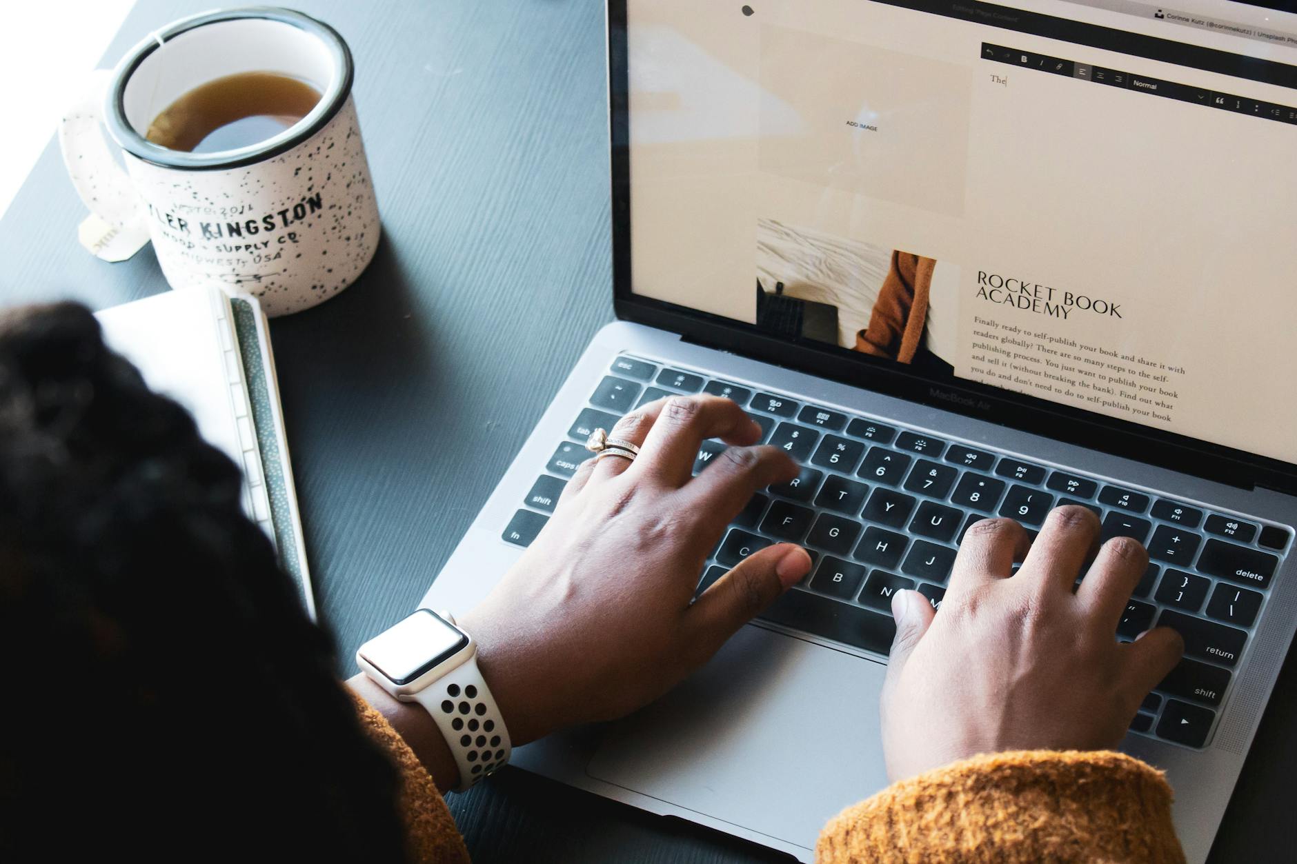 Close-up of hands typing on a laptop, enjoying coffee while working remotely.