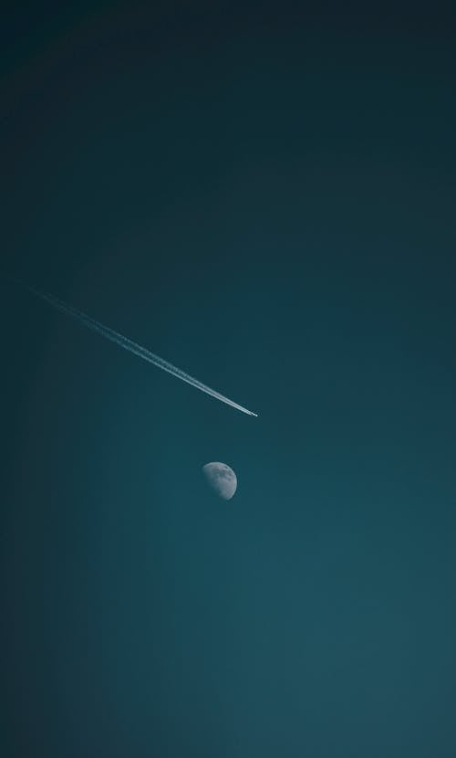 Free Airplane trail and luminous moon on dark sky Stock Photo