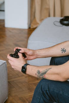 Tattooed person playing video games on a couch with a controller in hand.