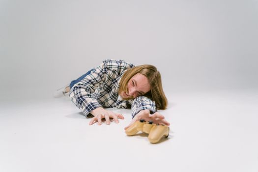 Young man in plaid shirt reaching for a controller on white studio floor.