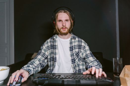 A young man focused on video gaming at home, wearing a plaid shirt and headset.