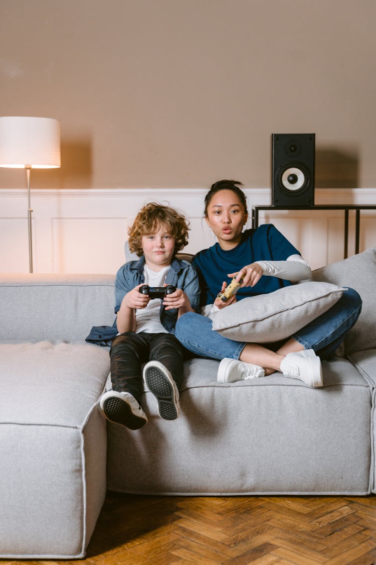 A Woman Playing Video Game With A Young Boy Sitting On The Couch