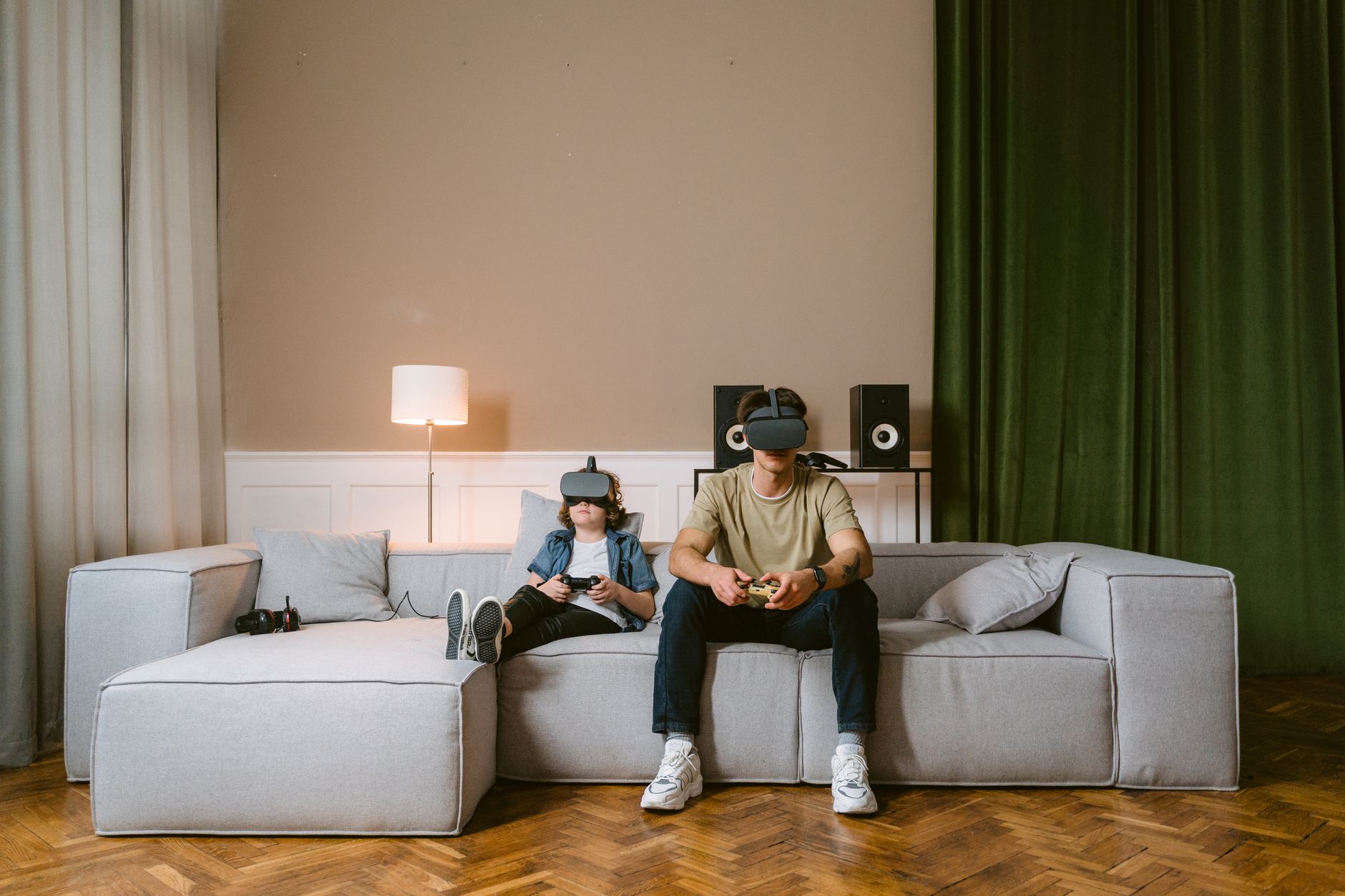 數位原生世代:孩子如何區分真實與虛擬世界 A man and child enjoying video games with VR headsets on a modern couch at home.