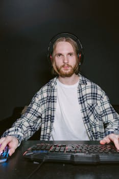 A focused young man playing video games indoors, equipped with gaming headphones and keyboard.