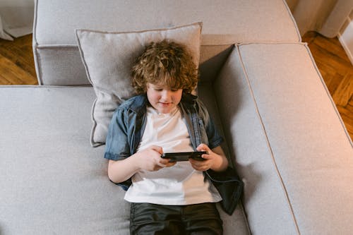 A Young Boy Lying on the Couch while Using His Phone