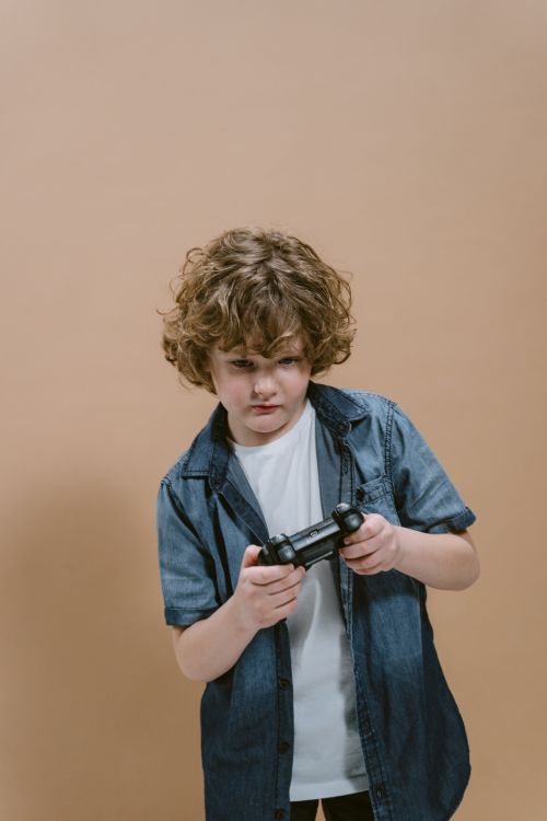 Free Curly-haired child focused on playing video games with a controller against a brown background. Stock Photo
