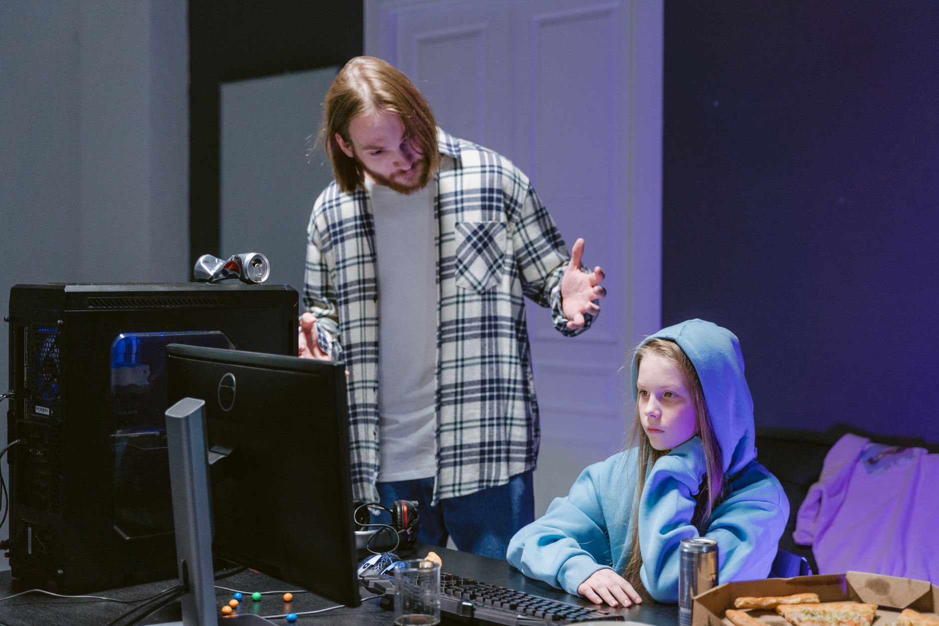 A father scolds his daughter playing video games on a computer, creating a tense moment.