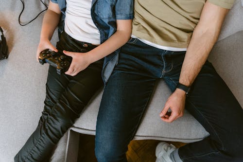 A Man in Blue Denim Jeans Sitting Beside a Boy Playing Video Game