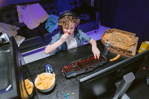High-Angle Shot of a Boy Playing Computer Video Game while Eating Pizza