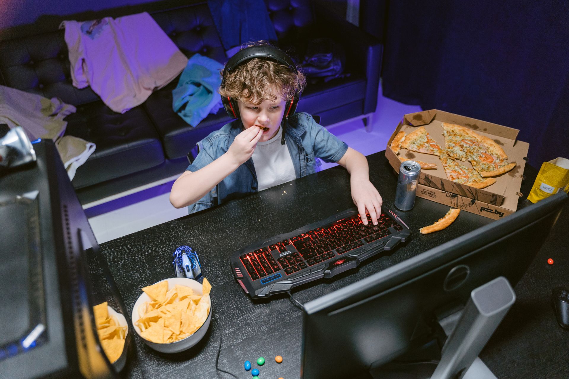 Boy playing video games with snacks and pizza by his side, enjoying leisure time.