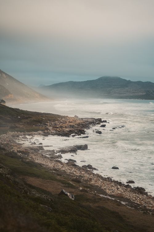 Free Captivating view of Cape Town's rugged coastline with crashing waves and misty mountains. Stock Photo