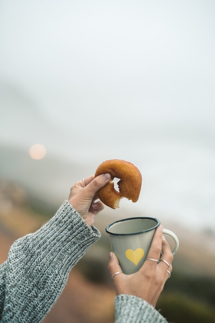 A Person Holding A Donut And A Cup Of Coffee