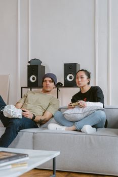 Young couple enjoying video games on a modern sofa indoors with gaming consoles.