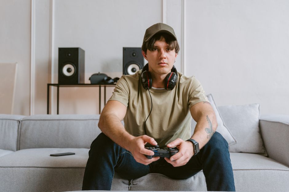 Casual scene of a young man playing video games on the couch with headphones and controller.