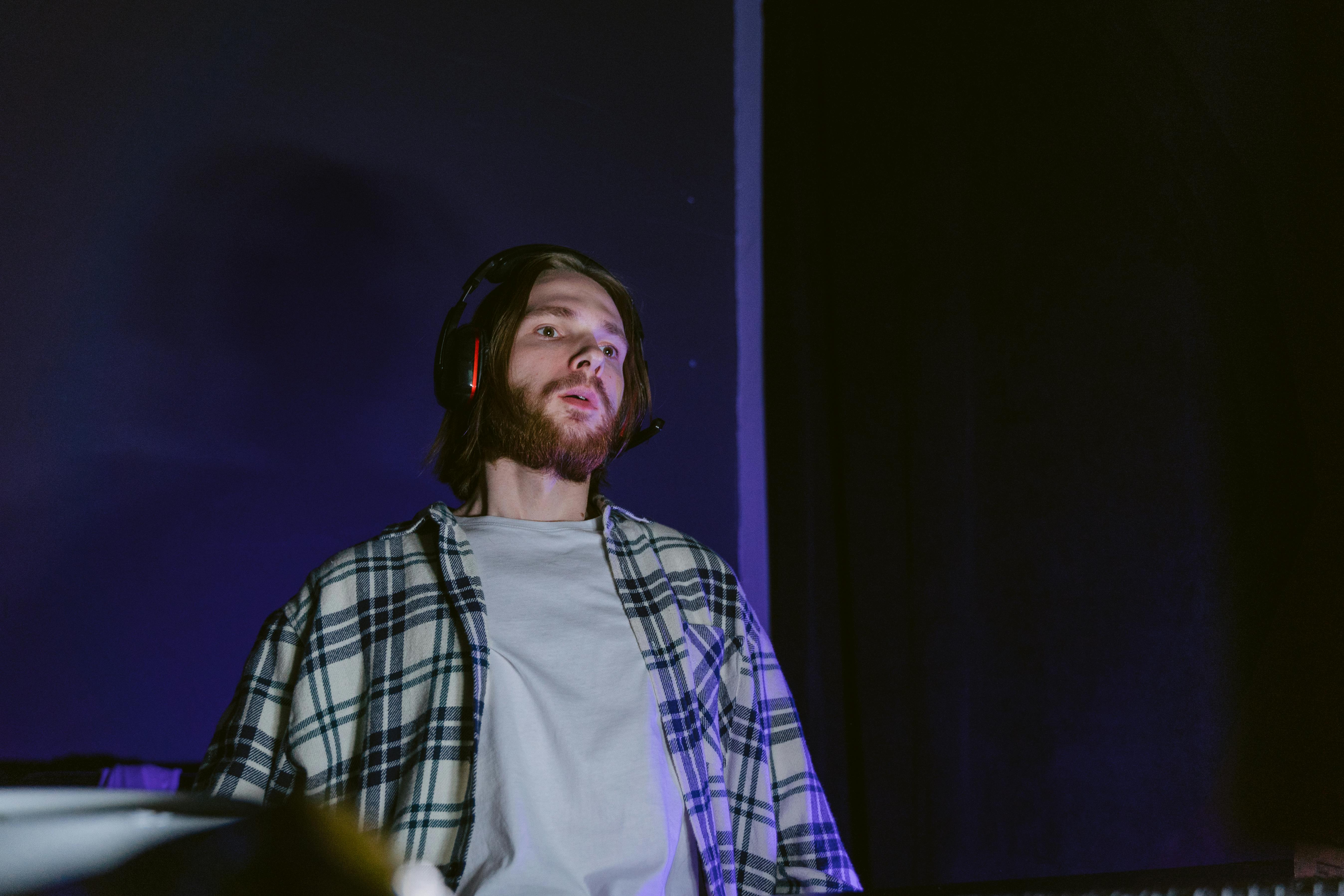 Bearded man in plaid shirt listening to music with headphones indoors.