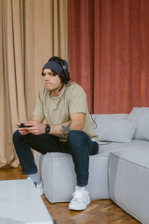 Free Adult man sitting on couch, focused on playing video games with a headset. Stock Photo