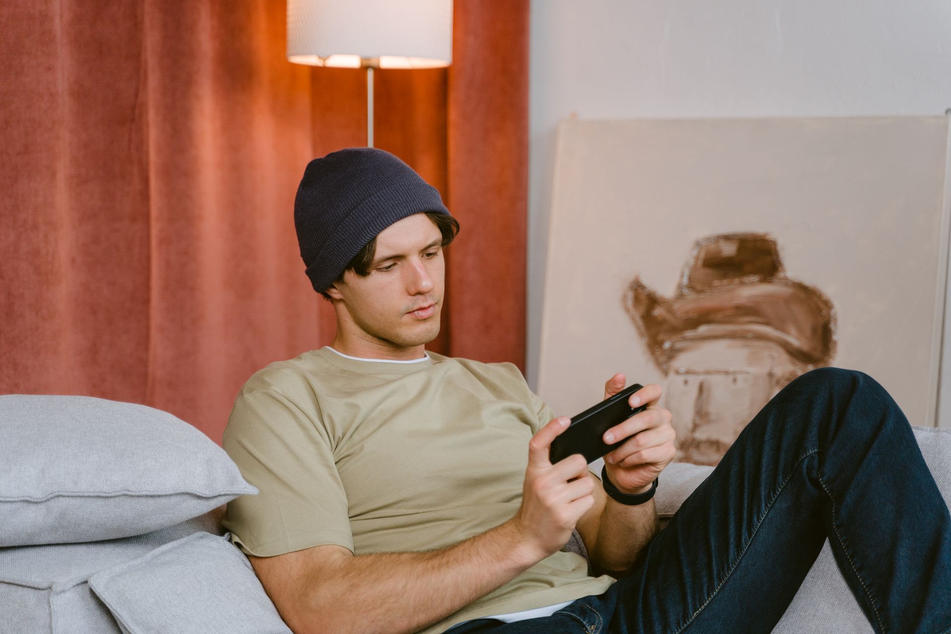A young man sits on a sofa playing video games with focus and relaxation.