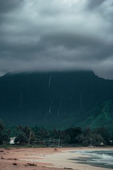 A moody coastal scene with mountains shrouded in clouds, capturing the essence of a rainy day at the beach.