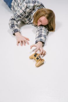 A person lying on a white floor reaching for a game controller, symbolizing gaming passion.
