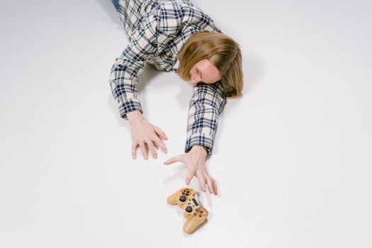 A young adult reaching out on a white floor to grasp a game controller, depicting focus and determination.