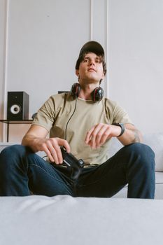 Young man sitting on sofa, gaming with headphones and controller indoors.