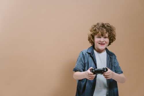 Free A happy child holding a game controller, enjoying video gaming indoors against a plain background. Stock Photo
