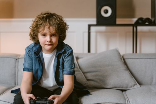 Free A child sitting on a couch playing video games with a controller indoors. Stock Photo