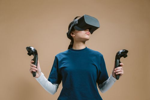 Free A young woman using a virtual reality headset and controllers, fully engaged in a gaming session. Stock Photo