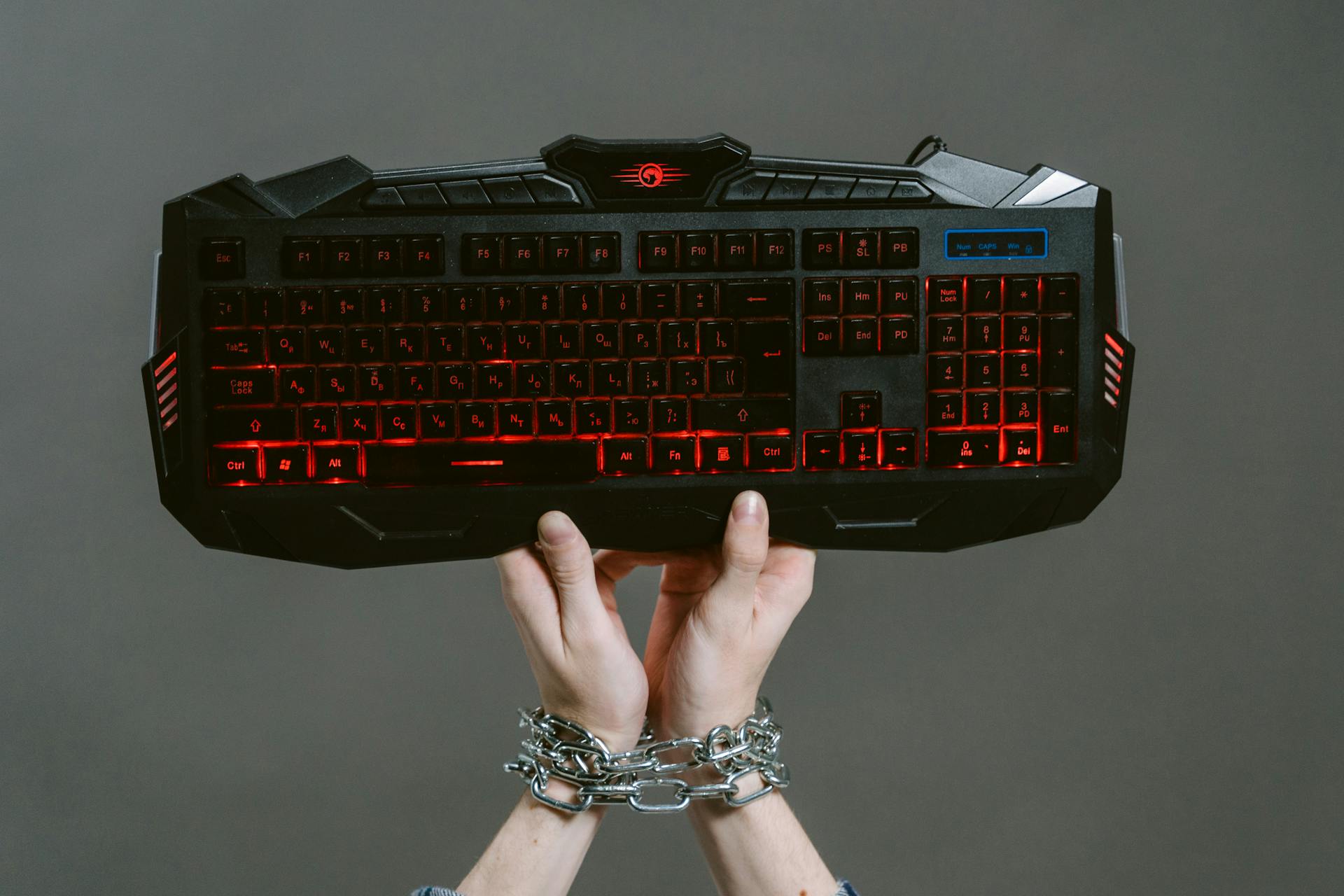 Hands in chains holding a gaming keyboard, symbolizing gaming addiction.