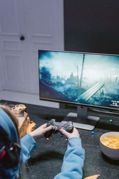 Focused teen playing a video game with controller at home, wearing headphones.