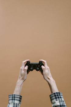A person holds a video game controller with both hands in front of a solid brown backdrop.