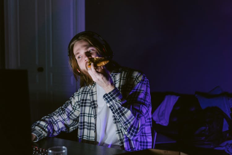 A Man Eating Pizza While In Front Of A Computer