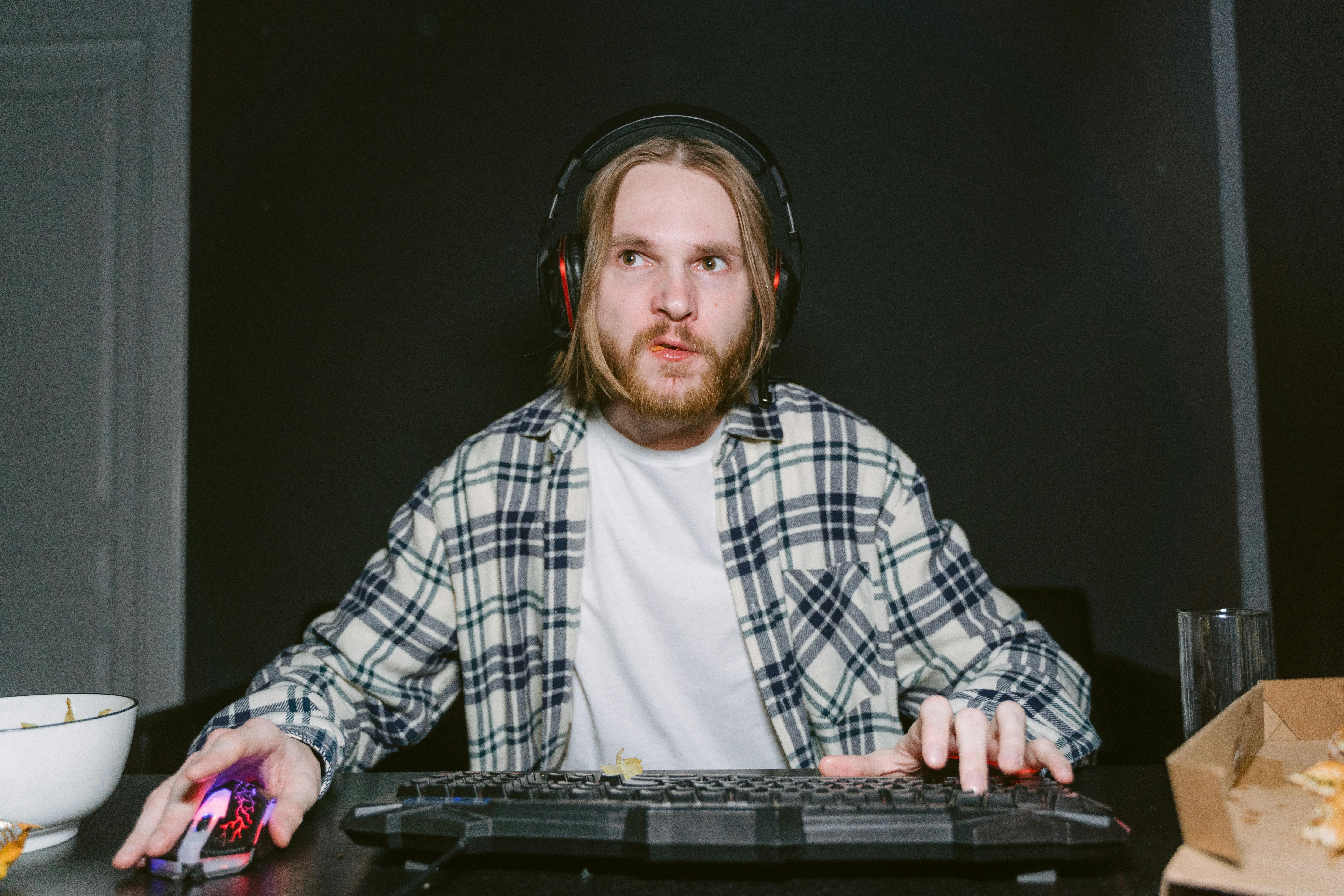 Man in plaid shirt intensely gaming indoors with headset and mouse.