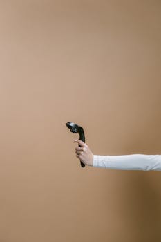 A hand in white sleeves holds a wireless VR controller against a brown background.