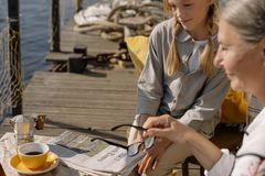 A grandmother and granddaughter enjoying leisure time by a dock with coffee and a newspaper.