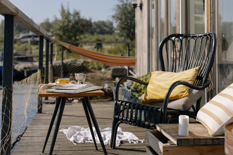 A Black Wooden Chair With Throw Pillows Beside A Table On A Porch