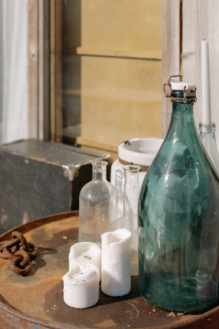 Empty Glass Bottles Beside Candles On A Rusty Surface