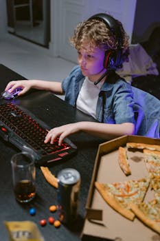 Child with curly hair focused on gaming, surrounded by pizza and gadgets. A modern day gaming scene.