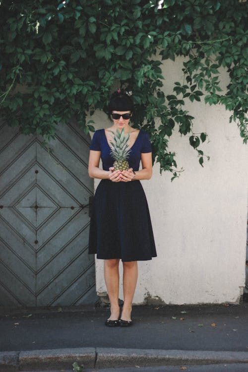 Woman Holding Pineapple Standing Beside Wall