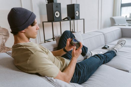 Casual young man playing mobile games on sofa with speakers in the background.