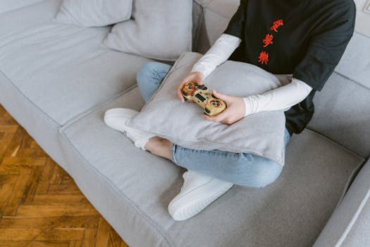Person sitting on a couch playing video games, symbolizing leisure and entertainment.