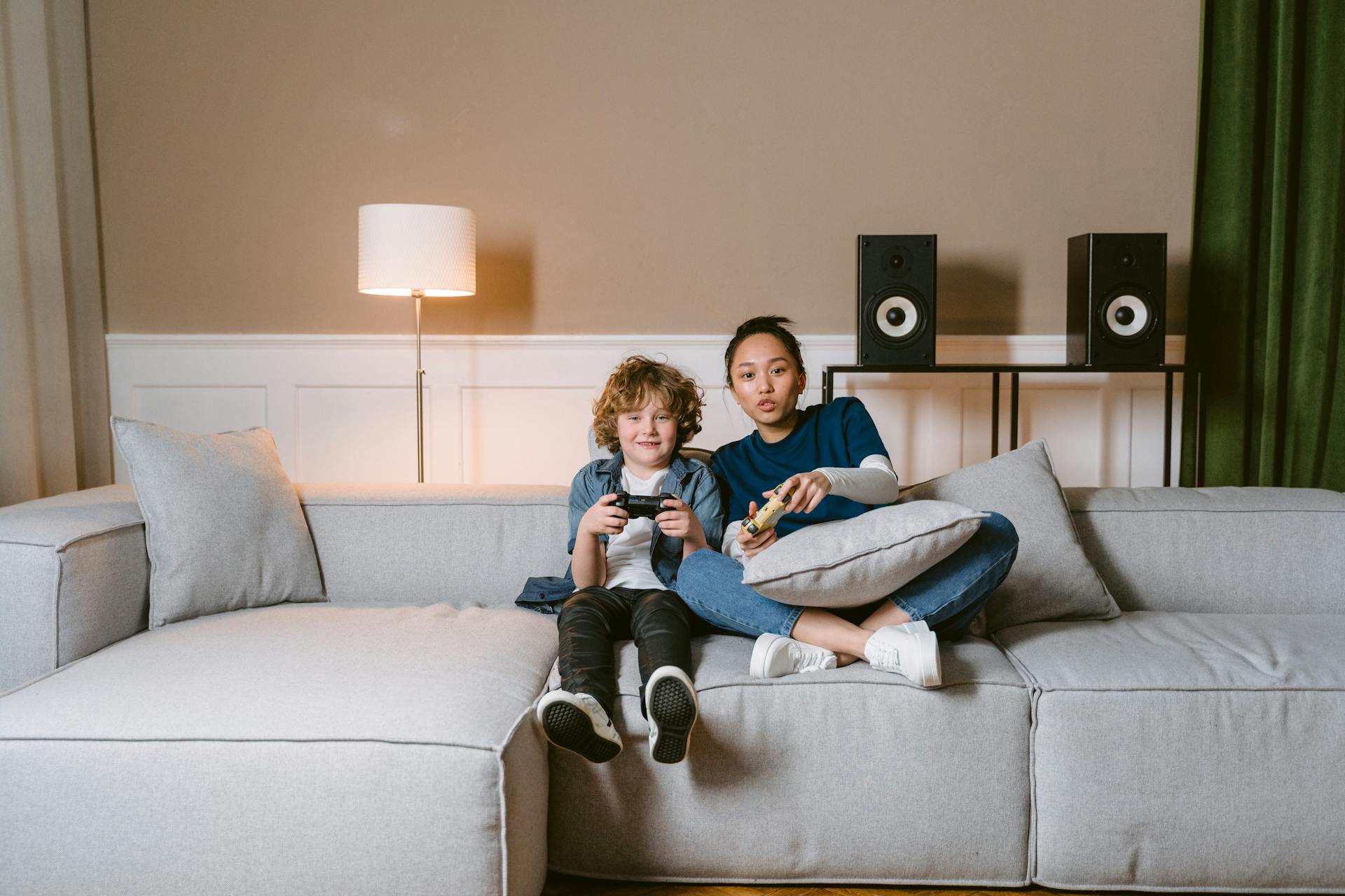 A Woman and a Kid Holding Video Game Controllers while Sitting on a Sofa