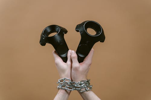 Free A Person with Chained Wrists Holding VR Controllers Stock Photo