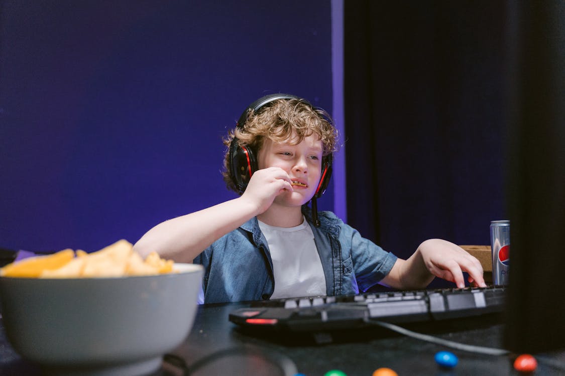 Boy Eating Chips in Front of a Computer