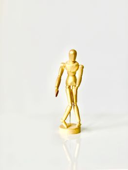 Wooden artist's mannequin standing on a reflective surface against a white backdrop. Ideal for art and design concepts.