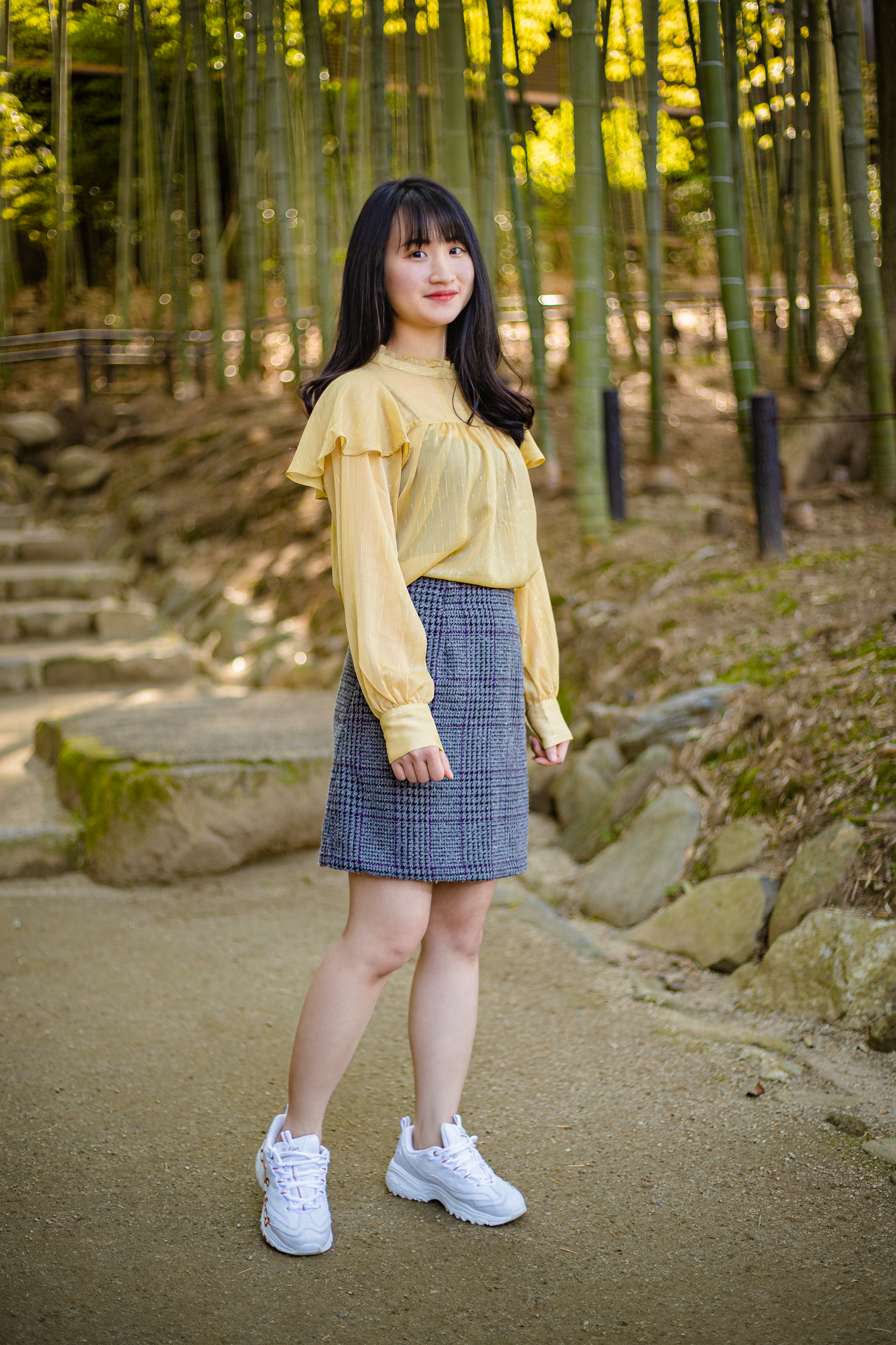 Stylish Asian woman in park, wearing fashionable outfit amidst bamboo grove.