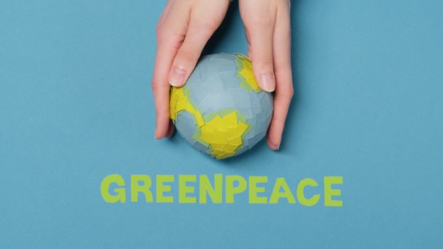 Hands gently cradling a paper Earth globe over a blue background with Greenpeace text below.