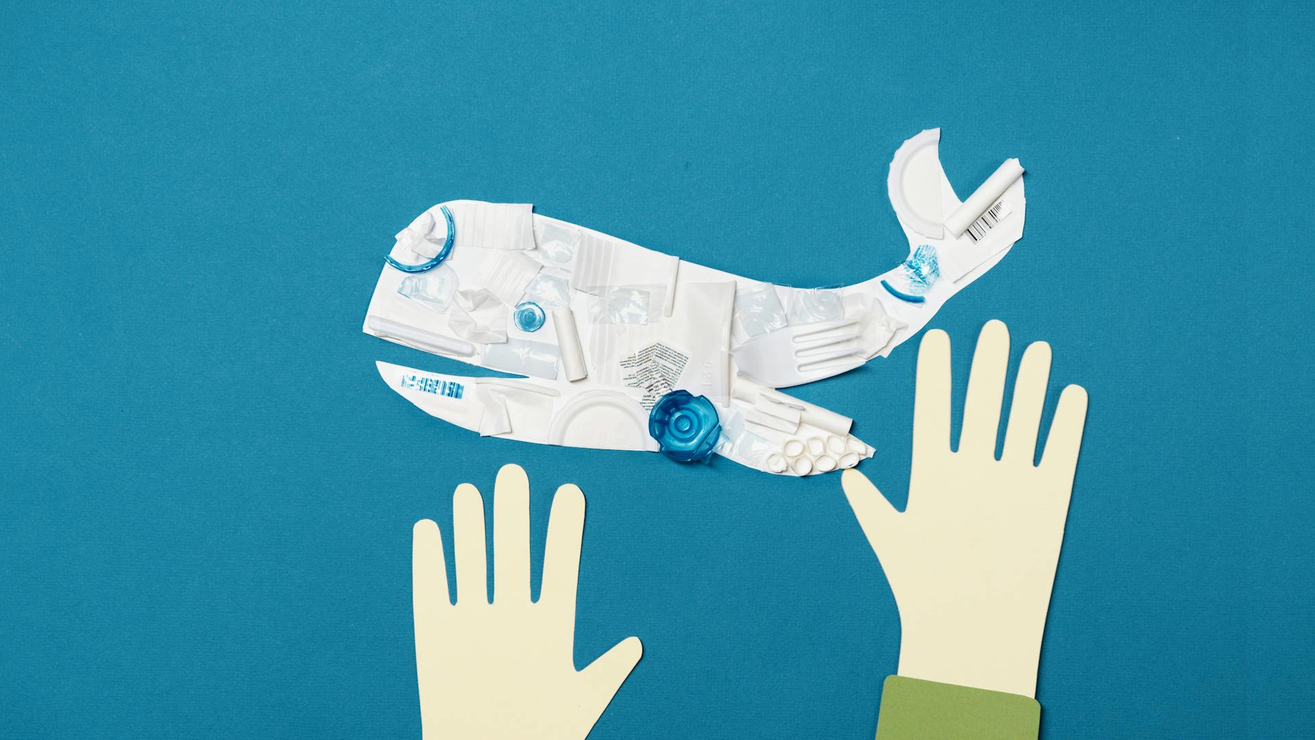 Paper cutout whale made from recycled materials on blue background, emphasizing environmental awareness.